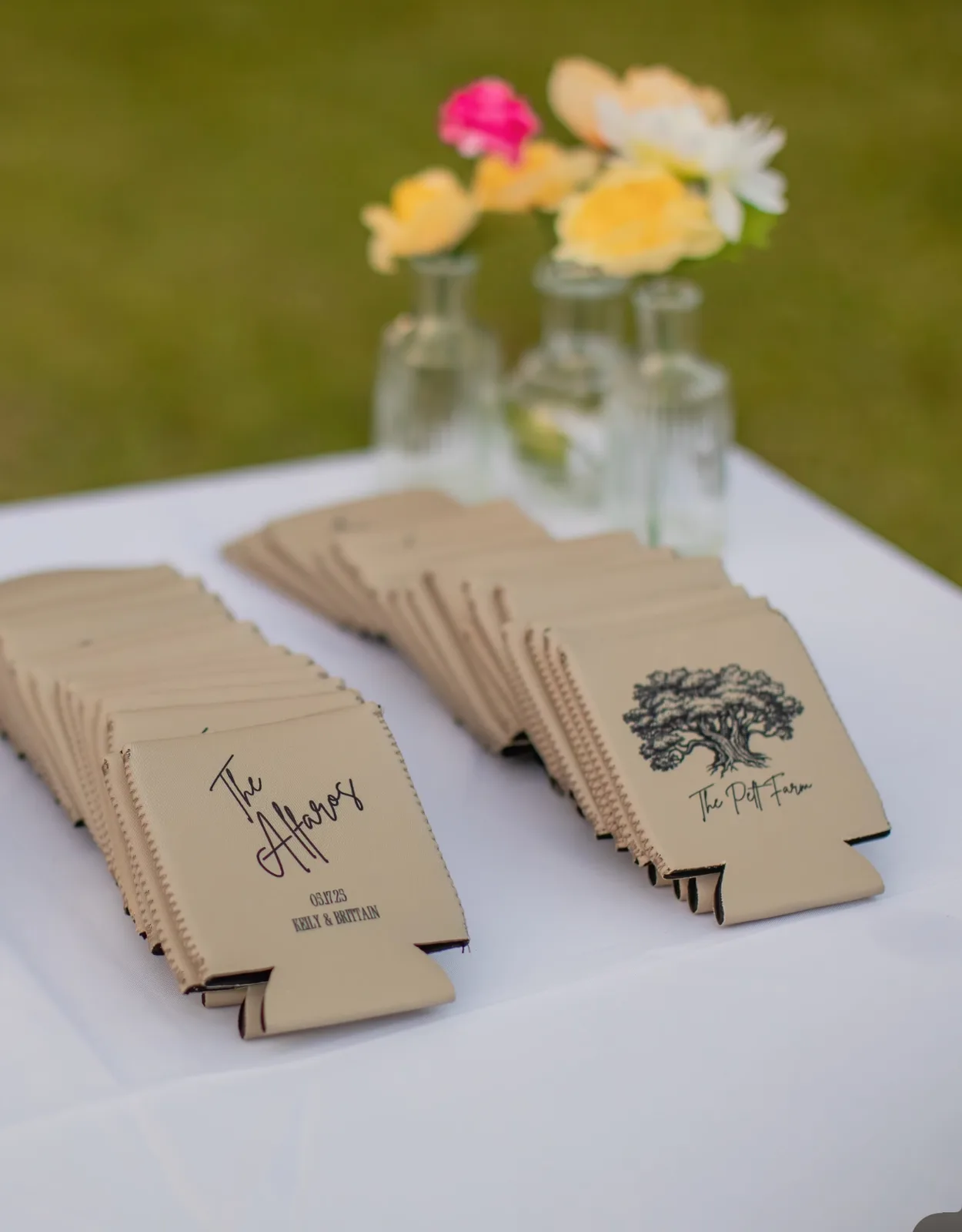 Cream can coolers on a wedding favor table, printed with "The Alfaros" in script and a live oak venue mark