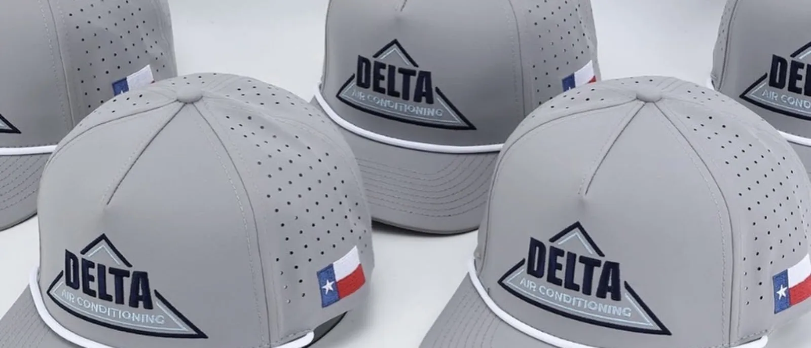 Close-up of grey Delta caps: the embroidered logo, the laser perforation and a Texas flag side hit